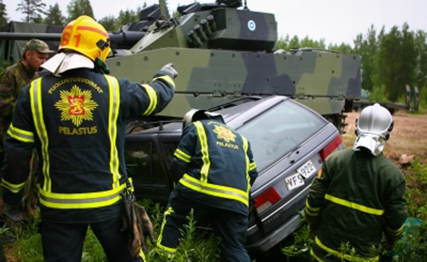 Pelastustehtävä, jossa pelastushenkilöstöä sekä ojaan ajautunut henkilöauto ja armeijan panssarivaunu.