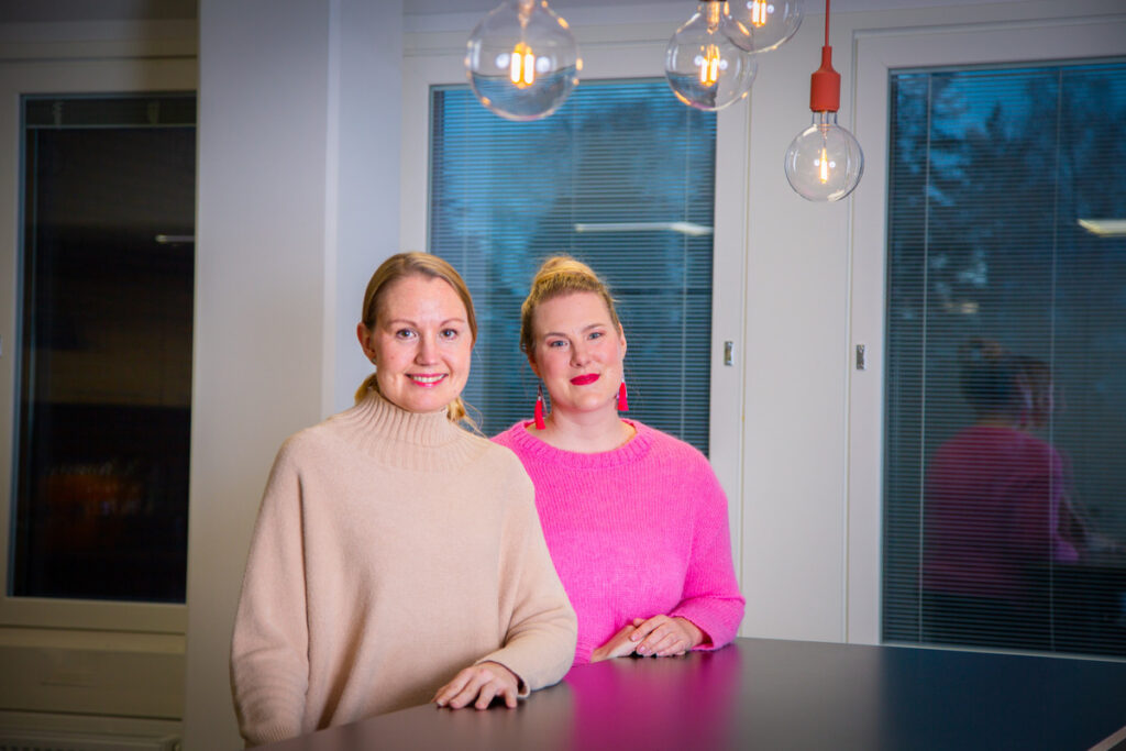 Henkilöstöasiantuntija Heidi Hyykoski ja viestintäpäällikkö Maria Hänninen seisovat pöydän ääressä.